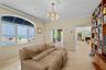 Large arched window with water and pool expanse, built-in floor-to-ceiling wood shelving, gold-tone contemporary chandelier, and light-colored stone f