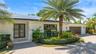 Single-story exterior featuring a light-toned stucco facade, rooftop solar panels, a paved brick driveway, a double-entry glass door, and integrated o