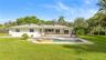 Rear exterior featuring a paver patio, in-ground pool with a raised stone-finish spillway, expansive grass lawn, and mature perimeter landscaping