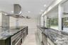 Kitchen featuring polished stone countertops, stainless steel appliances, a ceiling-mounted range hood, light-toned tile flooring, and large windows