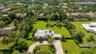 Aerial view of a sprawling property featuring a circular paved driveway, a multi-car garage, solar roof panels, a screened-in swimming pool, and expan