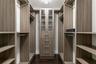 Custom walk-in closet featuring extensive wood-finish shelving, integrated hanging rods, a central stack of four soft-close drawers, and upper cabinet