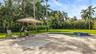 Expansive backyard featuring a stone-paver patio, swimming pool, raised tiled spa, manicured lawn, and mature palm trees