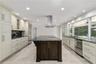 Kitchen featuring light-toned cabinetry, a dark-toned center island with a built-in cooktop, stainless steel range hood, stone-finish countertops, and