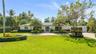Single-story exterior featuring a light-toned stucco façade, solar panels, paver driveway, manicured landscaping, and mature palm trees