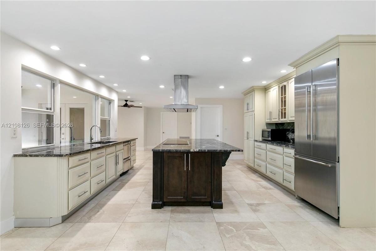 Kitchen featuring a central island with a stone countertop, custom cabinetry, stainless steel refrigerator, stone-tiled flooring, and recessed ceiling