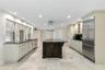 Kitchen featuring a central island with a stone countertop, custom cabinetry, stainless steel refrigerator, stone-tiled flooring, and recessed ceiling