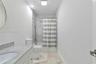Bathroom featuring a vanity with a stone-top counter, undermount sink, shower-tub combination with stone-style surround, and tile flooring