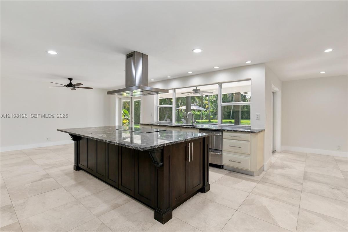Kitchen featuring a large central island with dark cabinetry, stone-finish countertops, stainless steel professional-grade range hood, recessed lighti