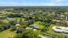 Aerial perspective of a sprawling property featuring a circular driveway, expansive manicured grounds, mature palm trees, and an in-ground swimming po