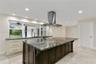 Kitchen featuring a large central island with dark cabinetry and stone-finish countertop, stainless steel ceiling-mounted range hood, light-colored pe