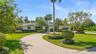 Single-story exterior featuring a paver circular driveway, solar panel installation, manicured landscaping with mature palm trees, and an attached two