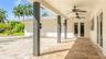Covered outdoor patio featuring light-toned paver flooring, dark wood-finish structural support columns, dual ceiling fans, and double glass-paned doo