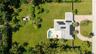 Aerial perspective featuring an expansive landscaped lot, paved circular driveway, integrated swimming pool with stone-surfaced patio, and a shingled 