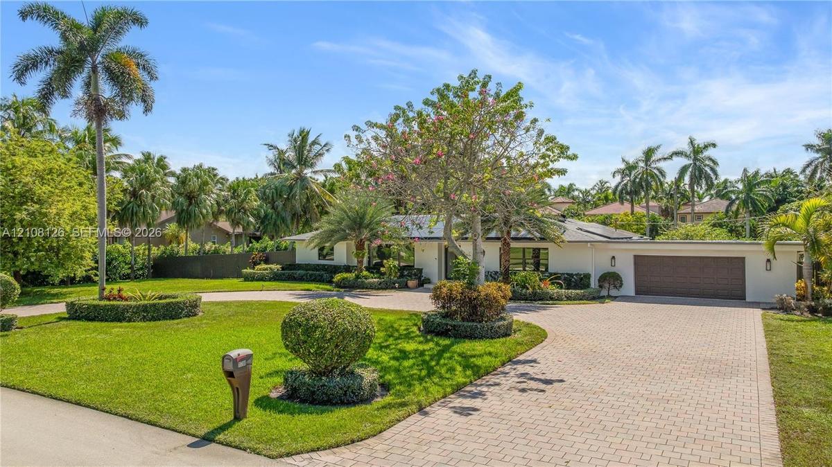 Single-story exterior featuring a paver driveway, an attached garage, and manicured landscaping with mature palm trees