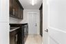 Dark-finish cabinetry with silver-tone hardware, stone-composite countertops, built-in tall pantry storage, and light-tone tile flooring