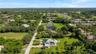 Aerial view of property featuring a circular paved driveway, expansive lawn, mature palm trees, and an in-ground swimming pool