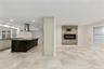 Kitchen featuring a dark-finish island with a countertop, stainless steel range hood, stone-finish fireplace, and neutral-tone tile flooring