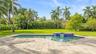 In-ground swimming pool with an attached spillover spa, blue tile detailing, expansive paver patio, and mature palm trees set against a private lawn
