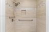 Walk-in shower featuring neutral stone-finish tile surround, integrated mosaic accent banding, built-in recessed niche, handheld shower fixture, and b