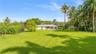 Expansive backyard featuring a sprawling manicured lawn, established palm trees, mature greenery, and a covered rear patio