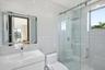 Bathroom featuring white tile wall cladding, a floating vanity with an integrated sink, an LED-illuminated mirror, a walk-in shower with a glass slidi