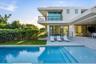 Modern exterior featuring a swimming pool, concrete patio, glass sliding doors, stone masonry accents, and a second-story metal railing balcony