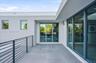 Modern balcony featuring expansive stone-tile flooring, floor-to-ceiling glass sliding doors, and a sleek metal horizontal-bar railing