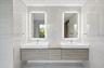 Floating dual vanity with wood-finish cabinetry, white integrated sinks, backlit rectangular mirrors, and recessed ceiling lighting, set against large