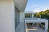 Modern architectural exterior featuring expansive covered balconies, metal railings, recessed lighting, and a ground-level outdoor kitchen with stone 