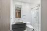 Floating vanity with a vessel sink, full-height tile wall, frameless glass shower enclosure, rainfall showerhead, and recessed lighting