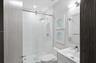 Walk-in shower with sliding glass enclosure and rainfall showerhead, white vanity with integrated basin, polished chrome fixtures, and wall-mounted va