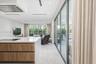 Open-concept kitchen featuring an island with a white countertop and wood-finish cabinetry, floor-to-ceiling glass sliding doors, recessed ceiling lig