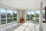 Floor-to-ceiling glass windows, recessed ceiling lighting, light-toned tile flooring, and a private balcony with metal railing