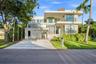 Modern three-story architecture featuring stone masonry accents, a covered parking structure, metal balcony railings, and expansive glass window panel