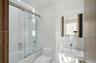 Bathroom featuring full-height stone-finish wall tile, a glass-enclosed shower with a rainfall showerhead, a wall-mounted medicine cabinet, and a cont