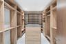 Custom walk-in closet featuring extensive wood-finish built-in shelving, hanging rods, an integrated center island with drawers, and a solid counterto