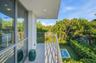 Covered balcony featuring tile flooring, horizontal cable railing, recessed lighting, and floor-to-ceiling glass paneling overlooking a private pool a