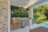 Outdoor kitchen featuring a stone-clad wall, built-in stainless steel grill, stone countertop with integrated sink, wood-finish cabinetry, and recesse