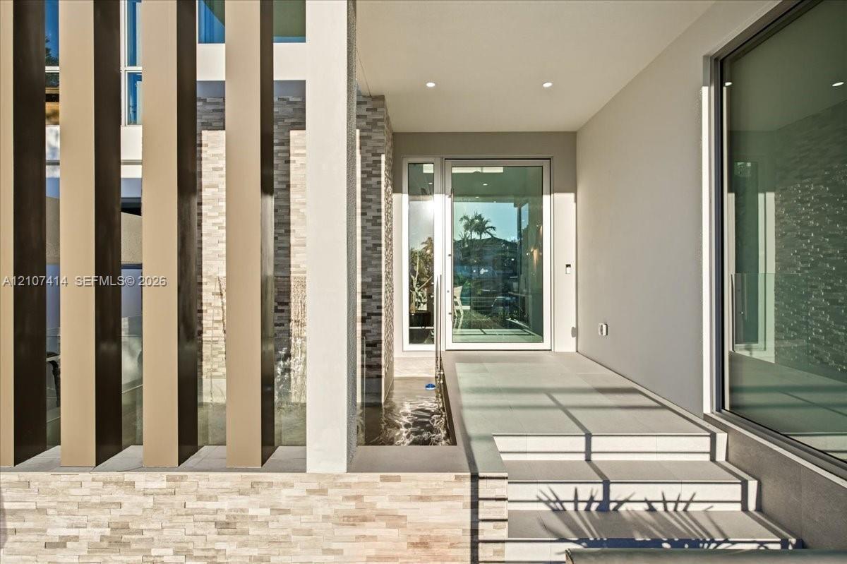 Contemporary entryway featuring vertical architectural screening, tiered stone masonry, recessed ceiling lighting, a water feature, and a glass-panele