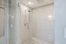 Walk-in shower featuring large-format stone wall tile, herringbone-patterned floor tile, a rainfall showerhead, a wall-mounted hand shower, and a glas