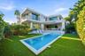 Modern two-story exterior featuring smooth stucco finish, stone accent pillars, expansive glass sliding doors, elevated balconies with metal railings,