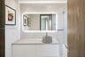 White vanity with a solid-surface countertop, cylindrical vessel sink, LED-backlit mirror, and full-height stone-finish wall tiling
