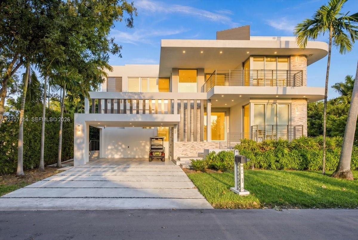 Modern multi-level exterior featuring smooth white stucco, stacked stone accents, two expansive balconies with metal railings, and a covered carport