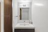 Floating vanity with an integrated basin, quartz countertop, minimalist wall-mounted lighting, frameless mirror, and large-format wall tile