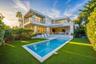 Modern two-story architectural exterior featuring expansive glass sliding doors, multiple balconies with metal railings, a rectangular swimming pool, 