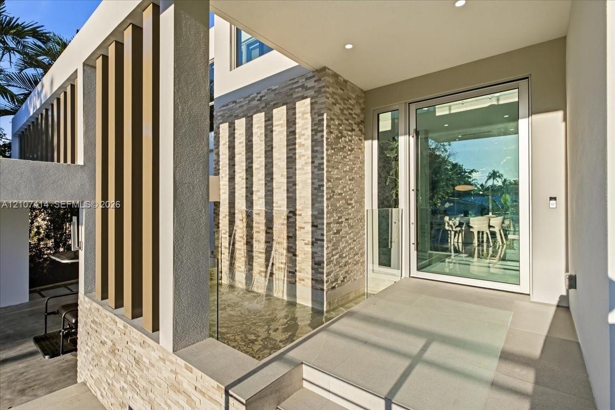 Modern entryway featuring a stacked stone facade, vertical architectural slats, an integrated water feature, recessed ceiling lighting, and a full-hei