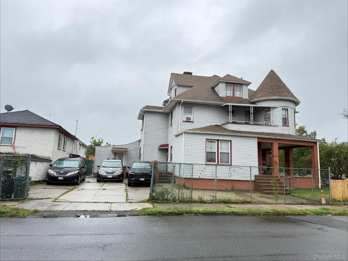 Multi-story exterior featuring a conical turret, wraparound covered porch, shingle-style roofline, and paved driveway