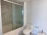 Bathtub with sliding glass enclosure, floor-to-ceiling stone-finish wall tile, one-piece dual-flush toilet, and chrome-finish hardware