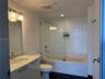 Bathroom featuring a stone-top vanity with an integrated sink, frameless glass shower panel, white tile tub surround, and three-light wall-mounted fix